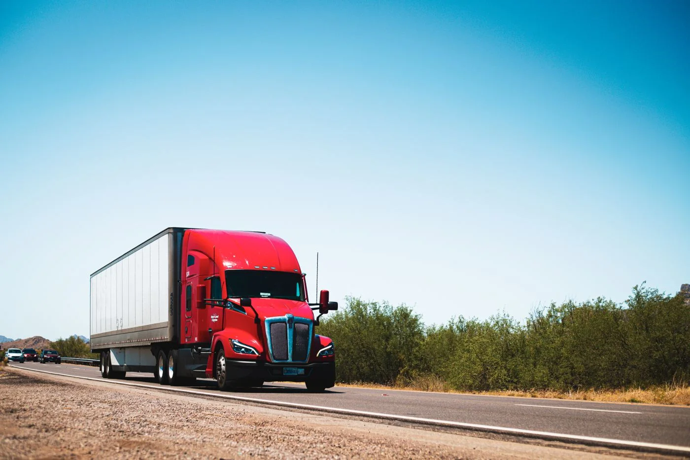 Red American semi-trailer truck driving on a highway beneath a clear sky